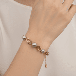 Złota bransoletka z kulkami i ogniwami na ręce modelki.