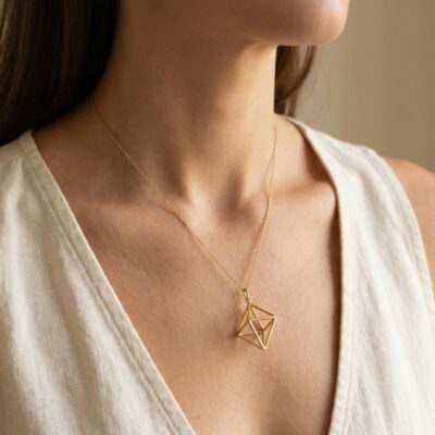 Złoty naszyjnik geometryczny w kształcie diamentu noszony przez modelkę.