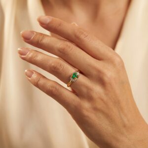 Złoty pierścionek ze szmaragdem i diamentami na dłoni