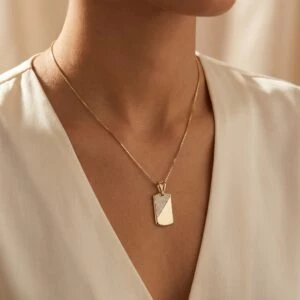 Złota zawieszka w kształcie prostokąta z cyrkoniami na modelce.