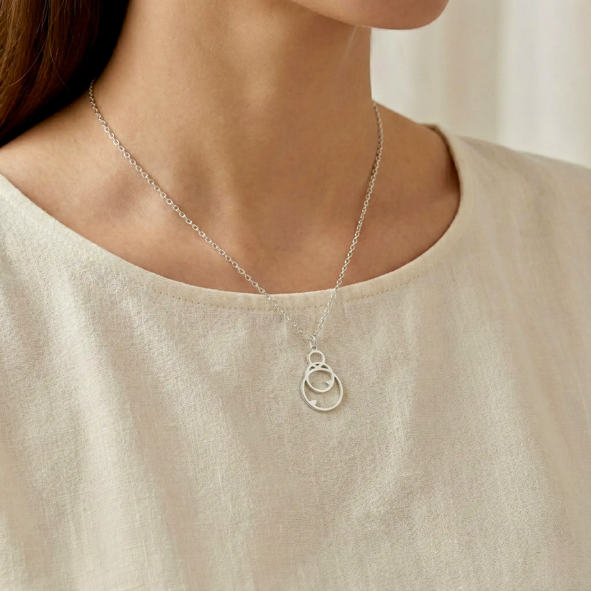 Srebrny naszyjnik z ażurowym wzorem, na jasnej bluzce.