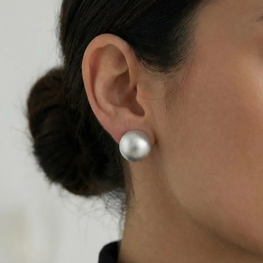 Srebrne kolczyki w kształcie kul, matowe, wykonane z próby 925, noszone przez modelkę.